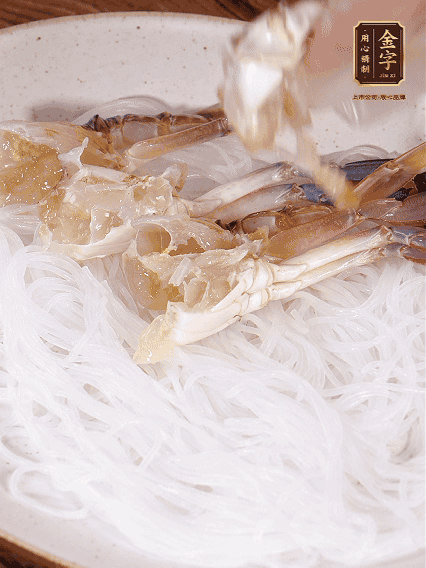 盤底墊上粉絲，擺上梭子蟹、火腿片，撒姜粒，淋上蒸魚豉油、花雕酒調(diào)味腌制15分鐘